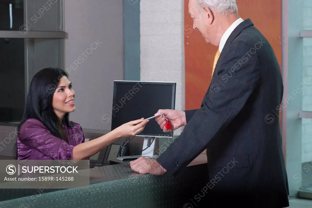 Hispanic receptionist handing card to businessman