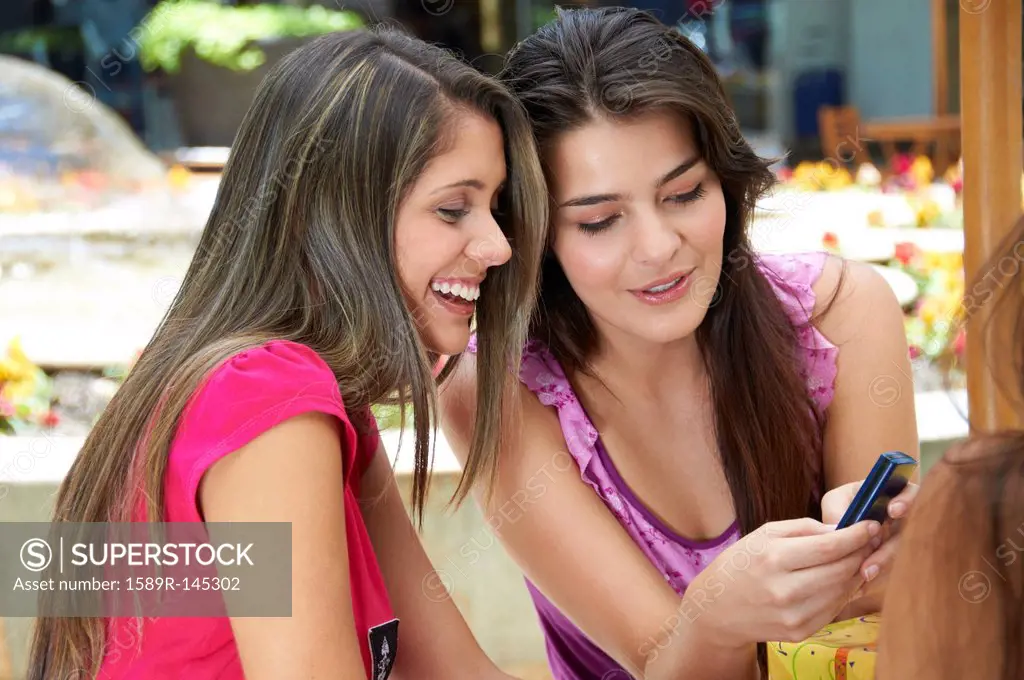 Hispanic friends text messaging on cell phone