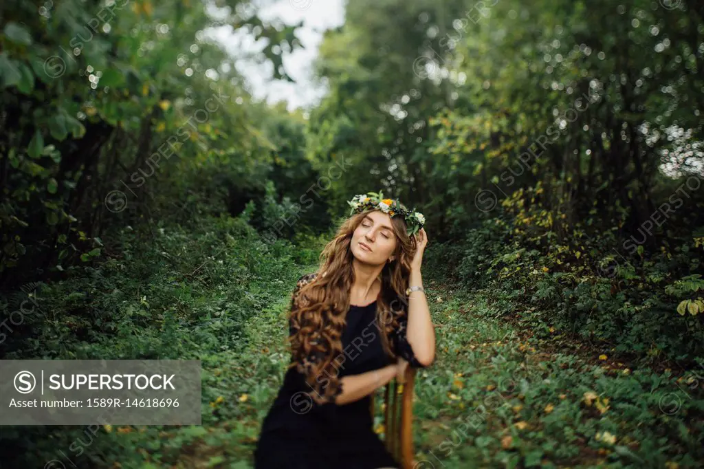 Middle Eastern woman wearing flower crown sitting on chair in woods