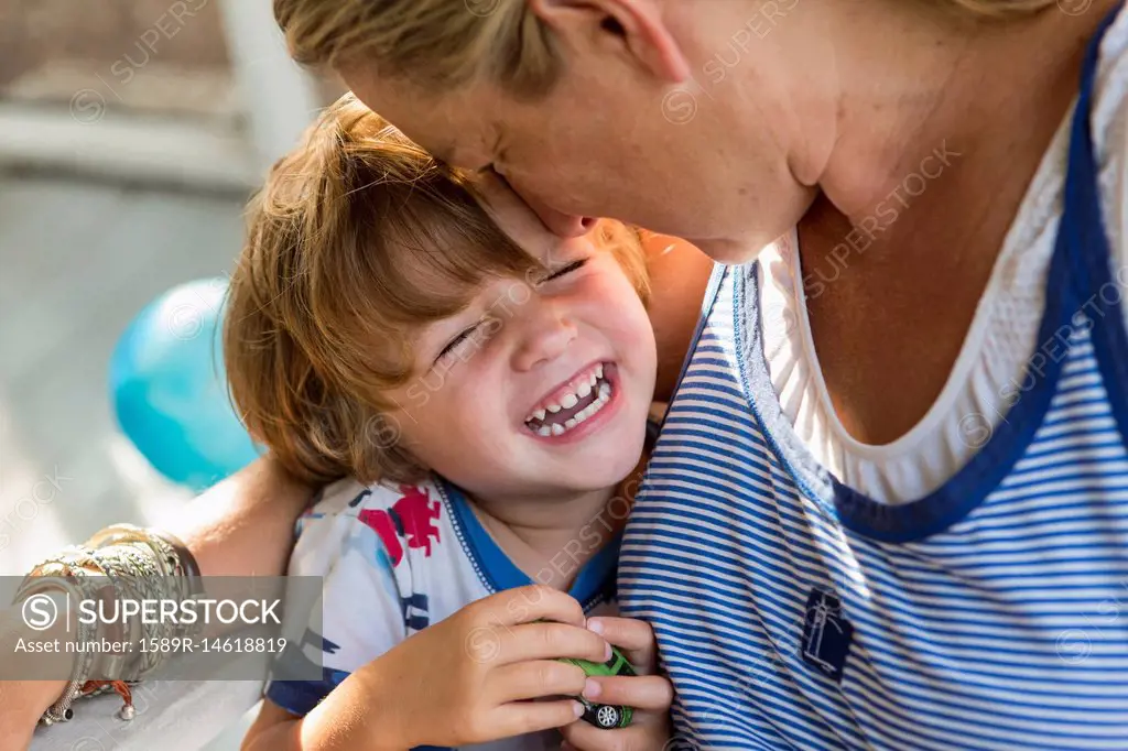 Caucasian mother hugging laughing son holding toy car
