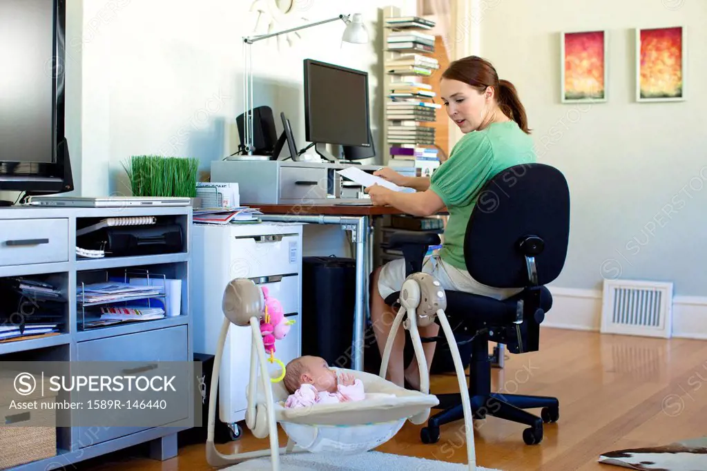 Caucasian mother working in home office with baby next to her