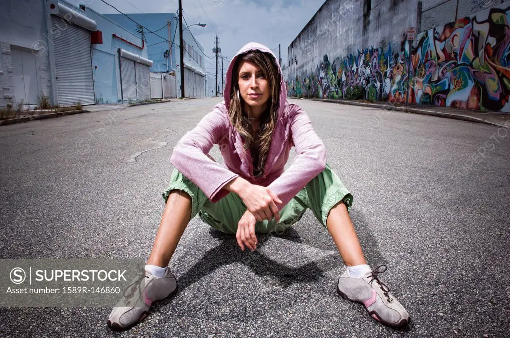 Hispanic woman sitting in alley with graffiti