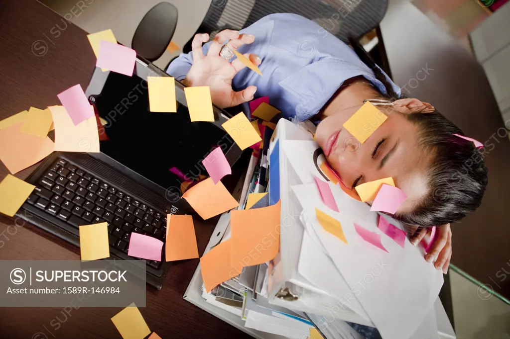 Hispanic businesswoman covered in sticky notes sleeping at desk
