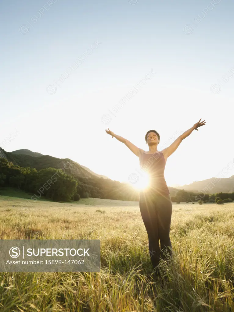 Mixed race standing in remote field with arms outstretched