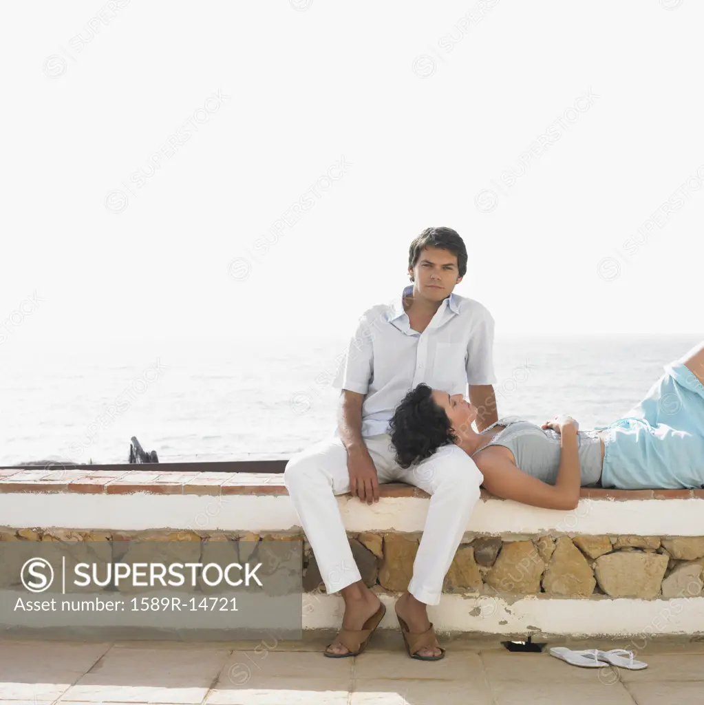 Young couple relaxing on stone wall near water