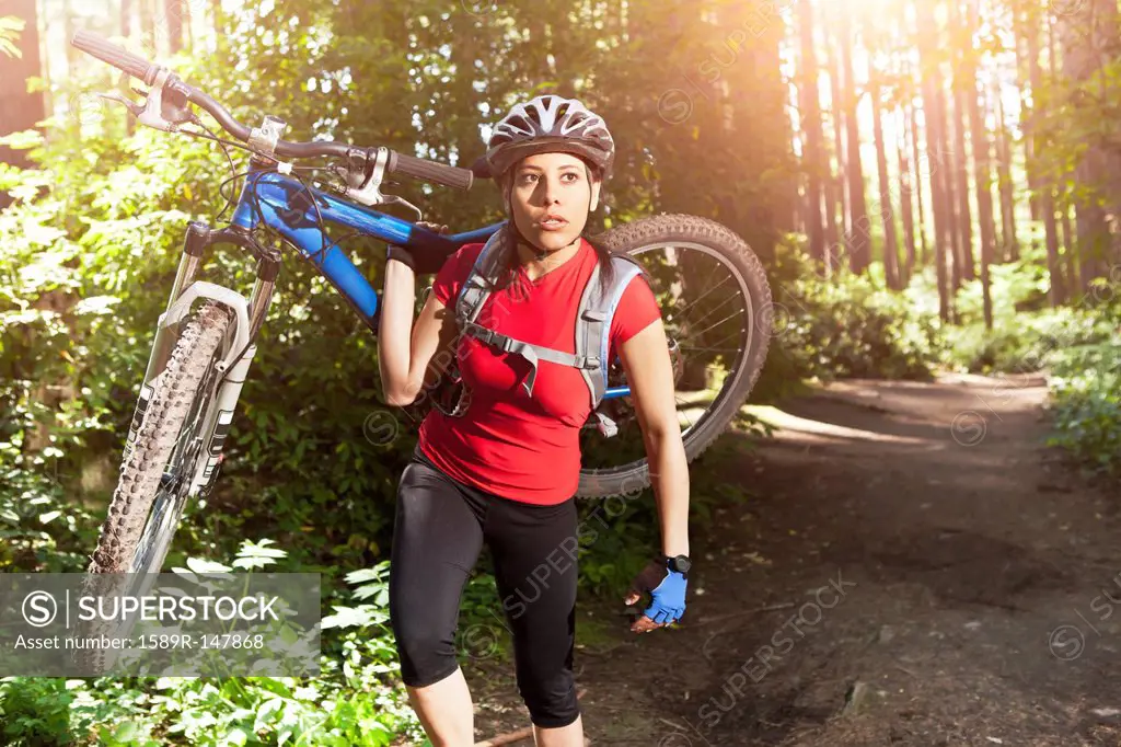 Hispanic woman carrying mountain bike in forest