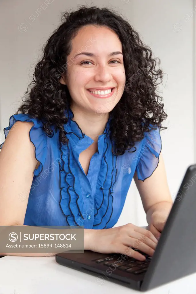 Smiling Hispanic businesswoman typing on laptop