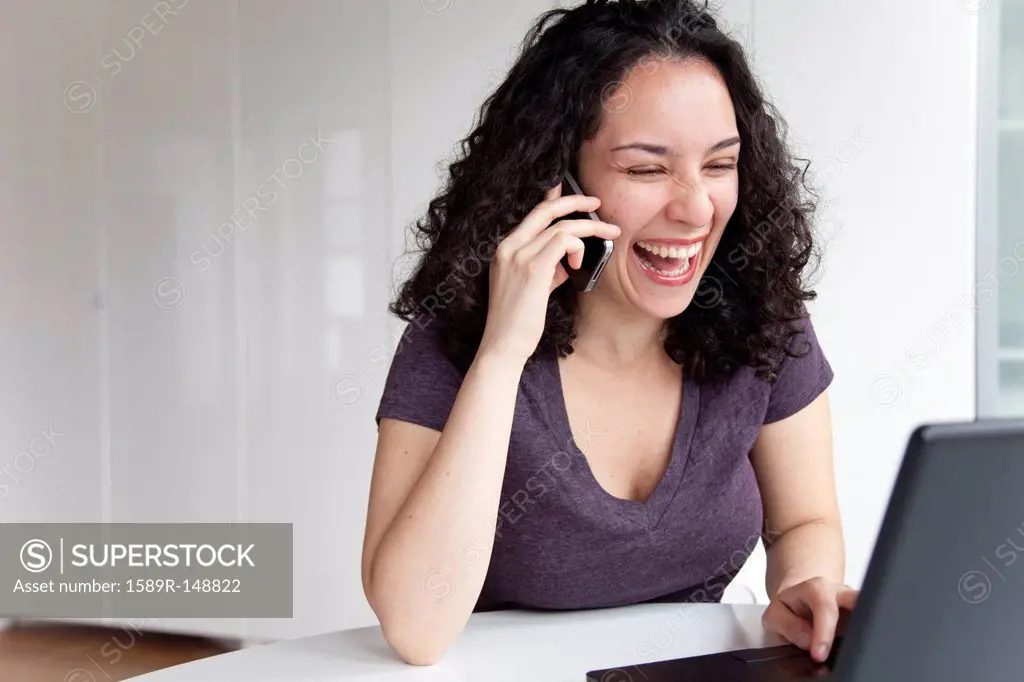 Hispanic woman talking on cell phone and using laptop