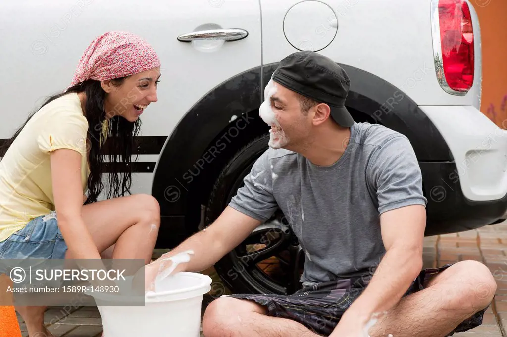 Playful Hispanic couple washing car together