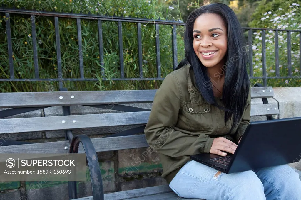 African American woman using laptop on park bench