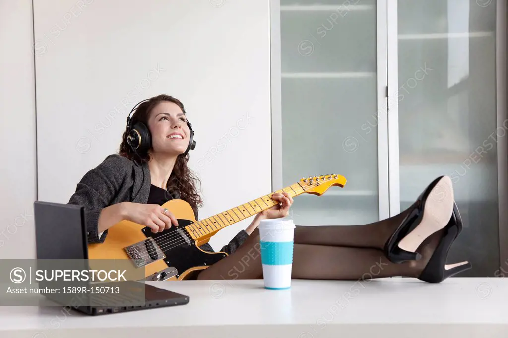 Businesswoman playing guitar at desk