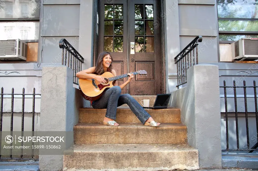 Mixed race woman sitting on front stoop playing guitar