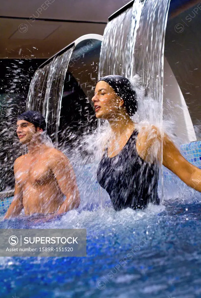 Hispanic couple enjoying waterfall in swimming pool
