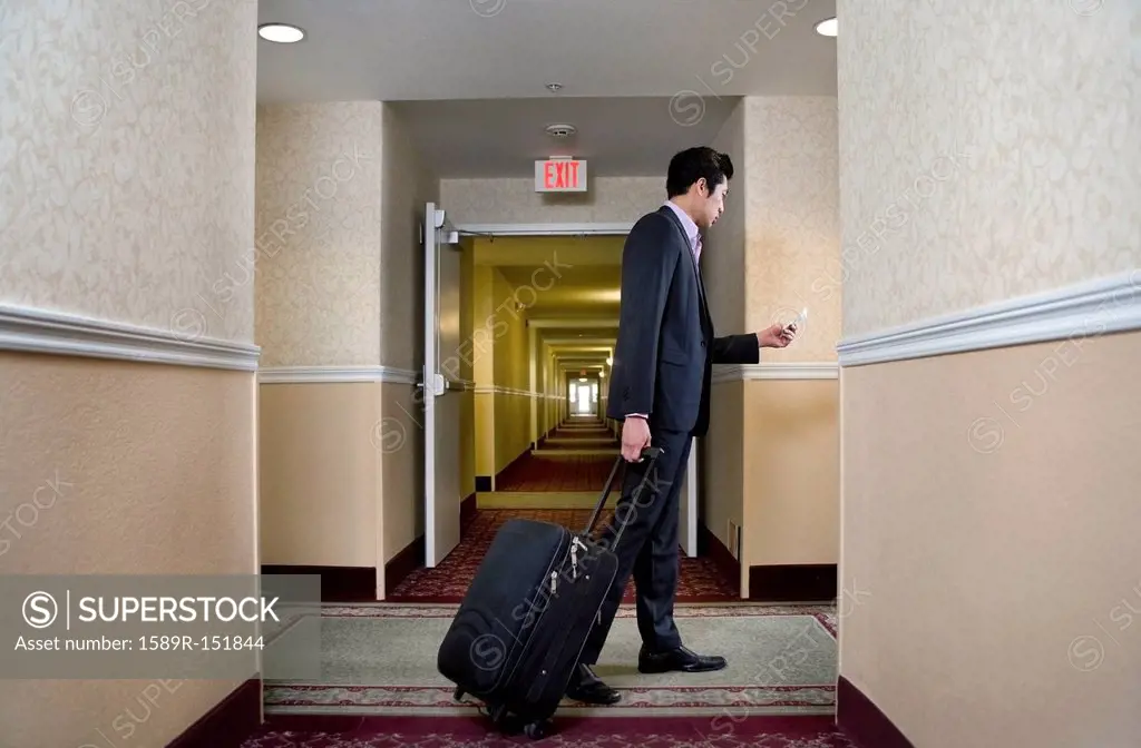 Asian businessman pulling suitcase in hotel
