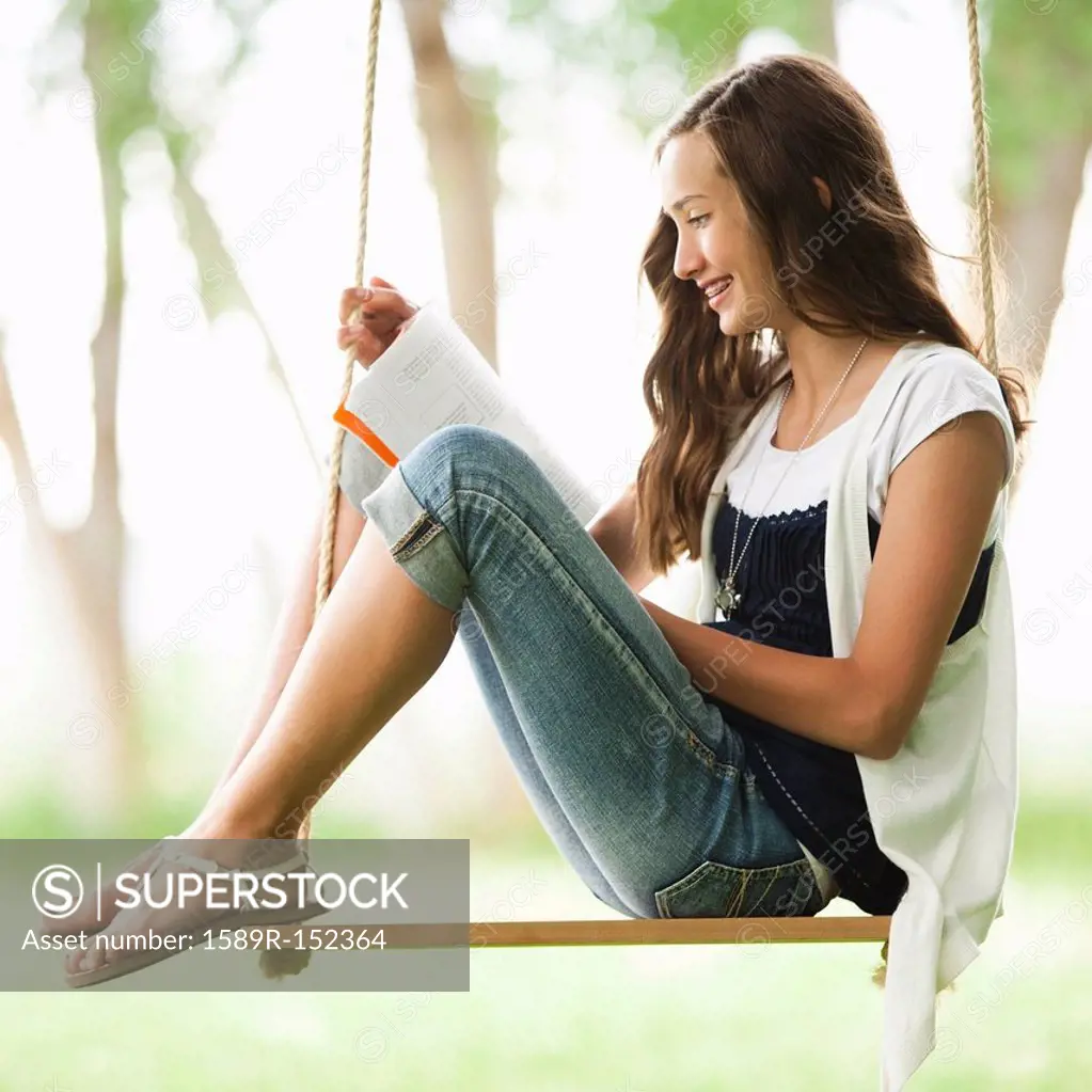 Caucasian girl reading book on swing