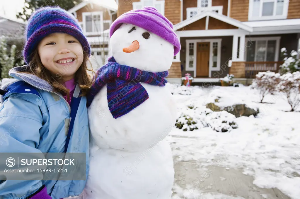 Portrait of girl with snowman in front yard