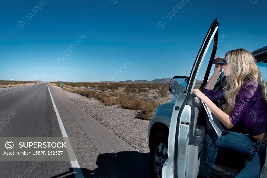 Caucasian woman parked on roadside using binoculars