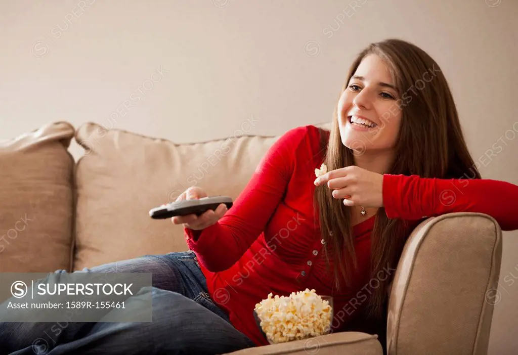 Caucasian woman watching television and eating popcorn