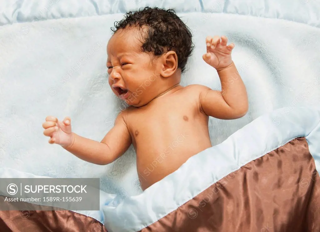 Mixed race newborn baby laying on blanket crying