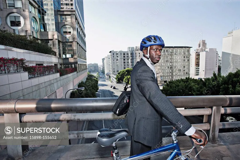 Businessman pushing bicycle over urban bridge
