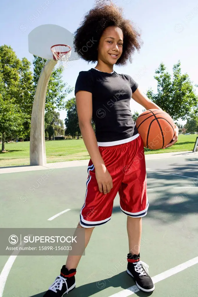 Smiling teenage girl holding basketball on court