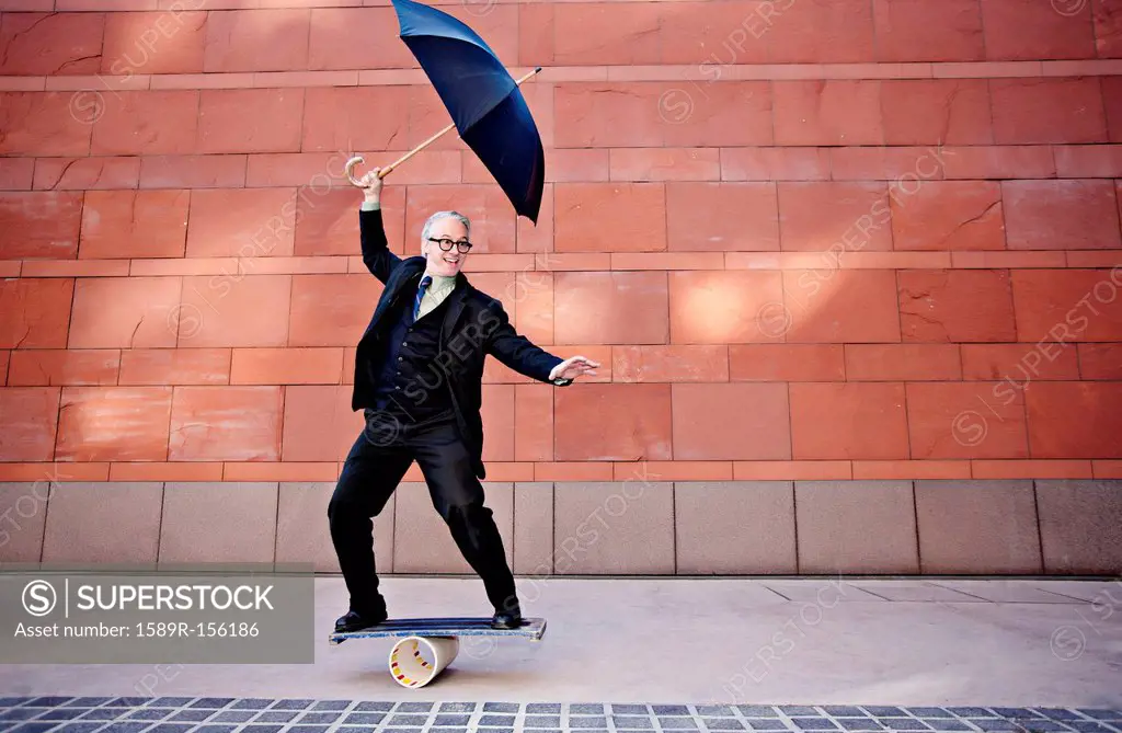 Caucasian businessman holding umbrella and balancing on board