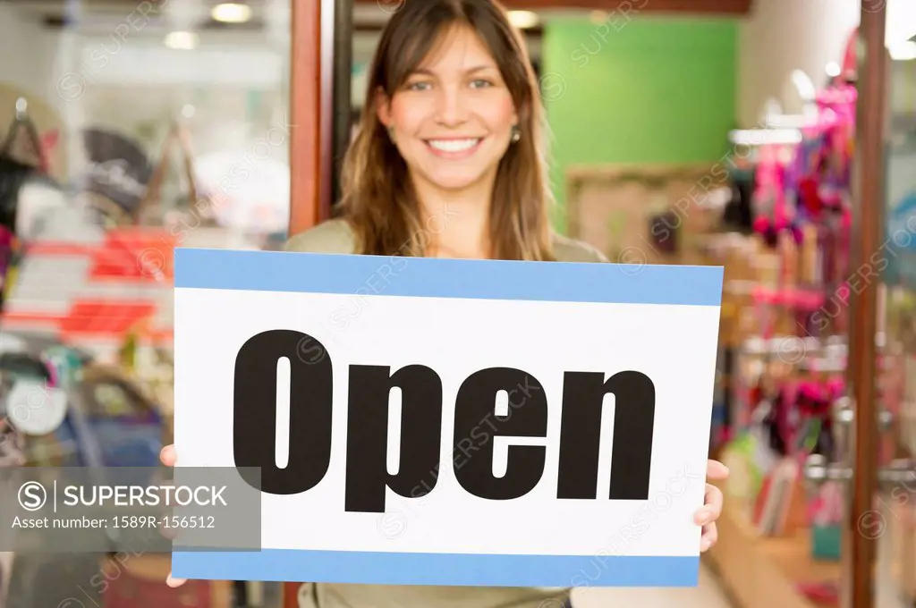 Hispanic woman holding open sign in store