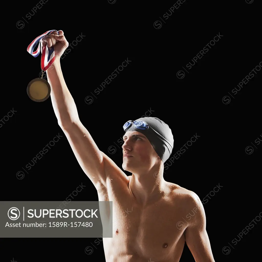 Caucasian teenage boy in swim cap and goggles holding medal