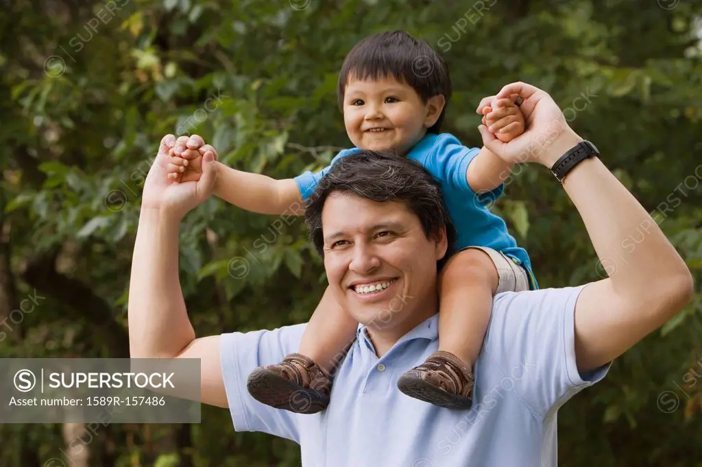 Hispanic father carrying son on shoulders