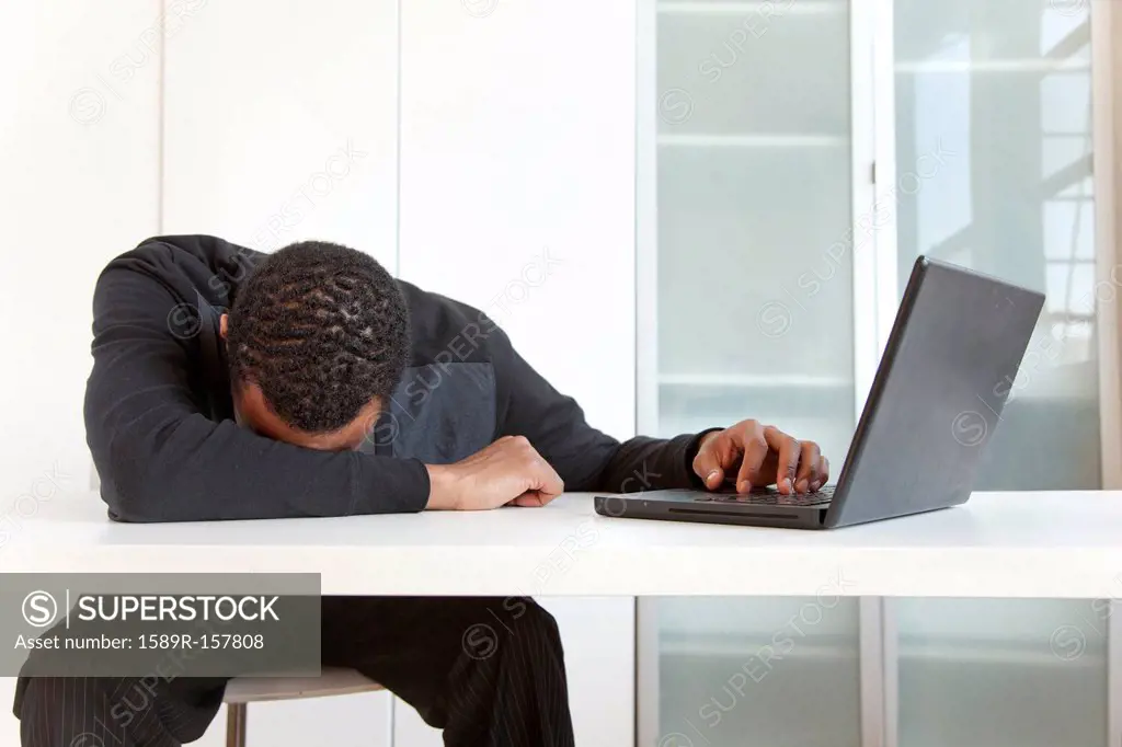 Tired Black businessman sleeping near laptop