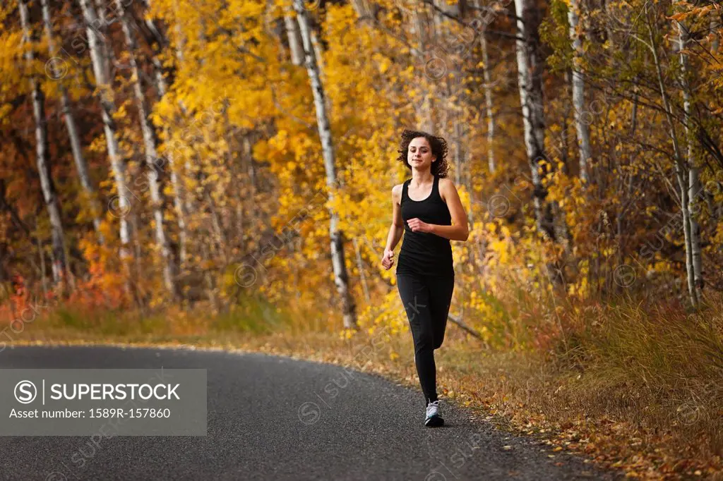 Caucasian woman running along autumn road