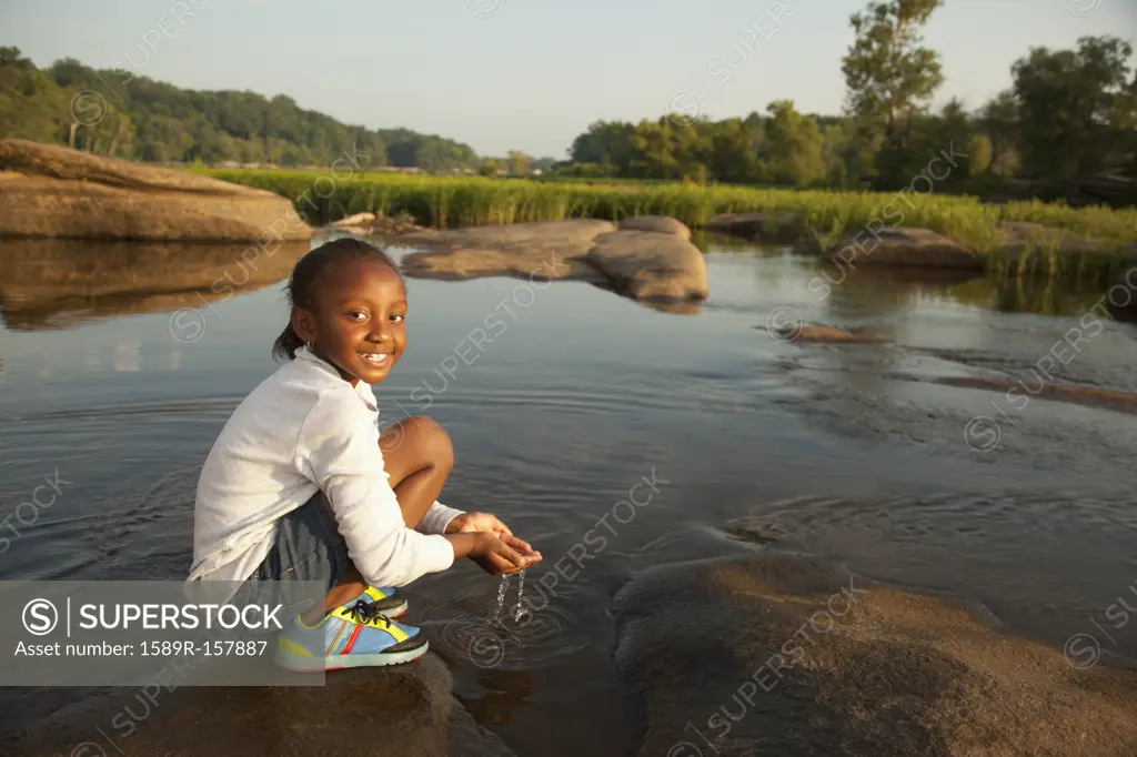African American girl scooping water from river