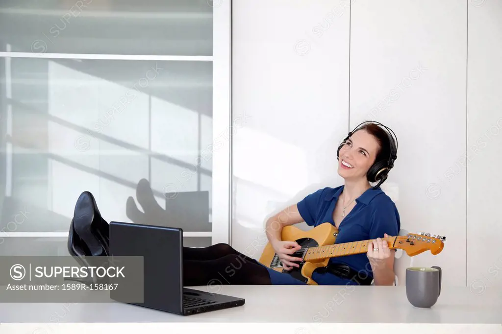 Caucasian businesswoman playing guitar at desk