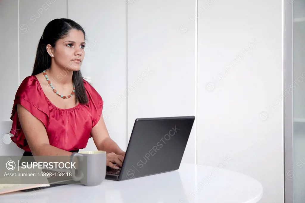 Hispanic businesswoman typing on laptop in office