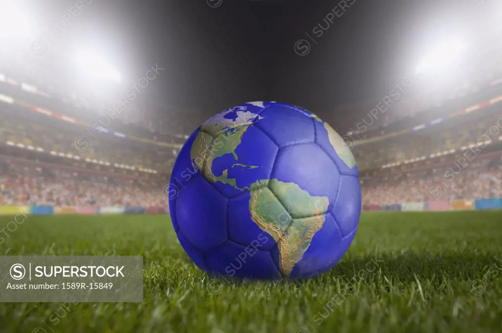 Soccer ball painted like a globe resting on grass in large stadium