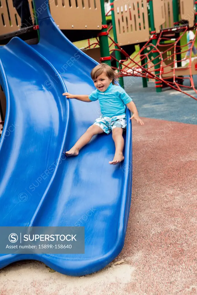 Mixed race boy sliding down slide in playground