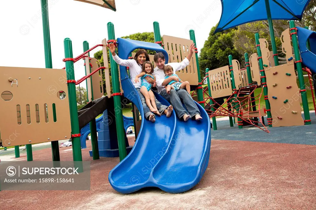 Family sliding down slide on playground