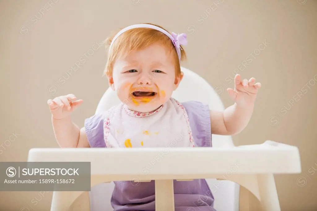Caucasian baby girl crying in high chair