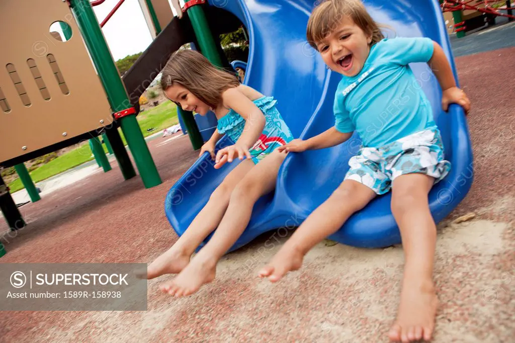 Brother and sister sliding down slide on playground