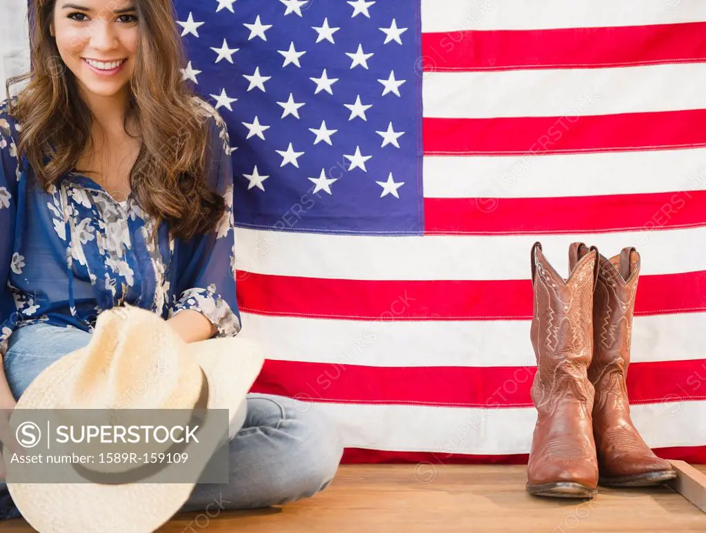 Hispanic woman holding cowboy hat and sitting next to American flag