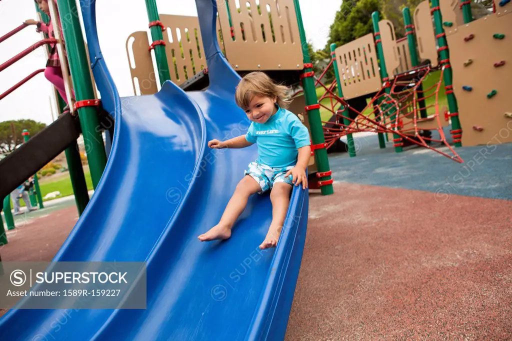 Mixed race boy sliding down slide on playground