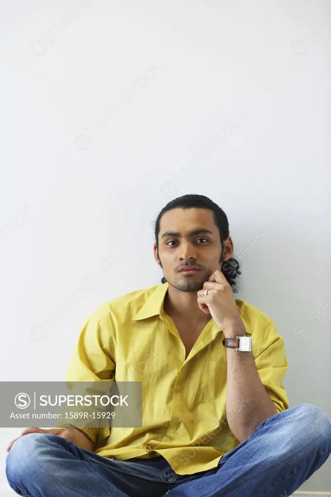 Portrait of man sitting on floor with hand on face