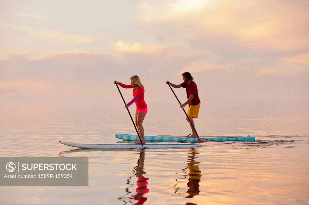 Caucasian couple standing on paddle boards