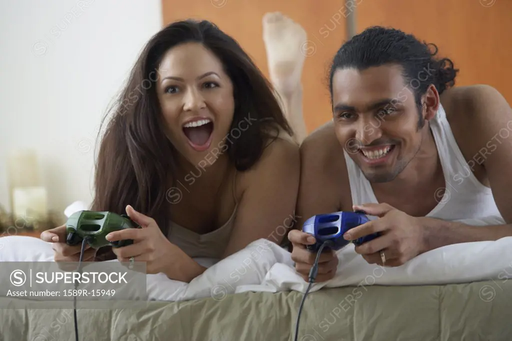 Couple laying on bed playing video games