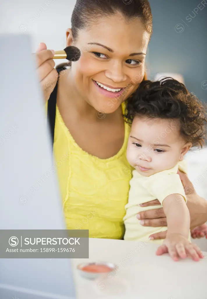 Mixed race other holding baby and putting on makeup