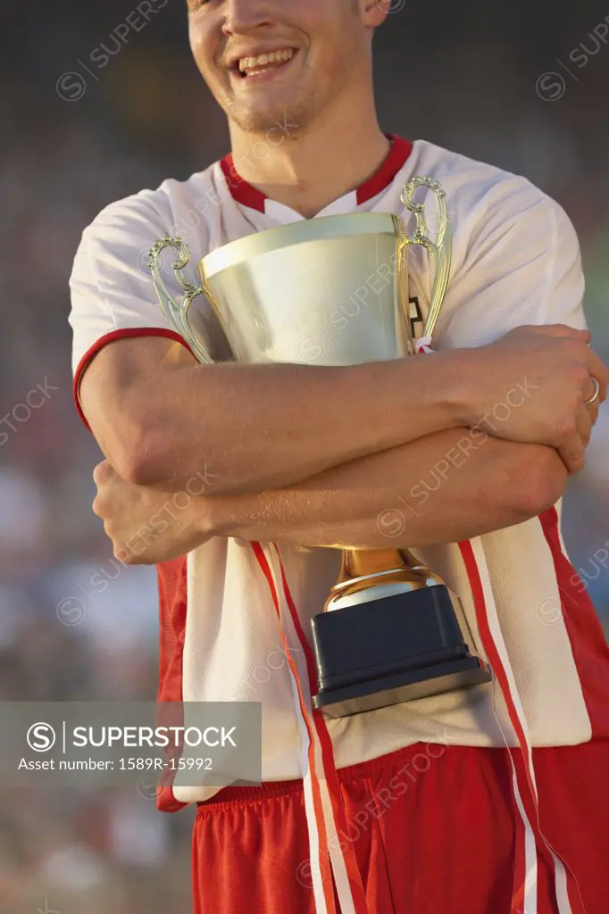 Male soccer player triumphantly hugging trophy