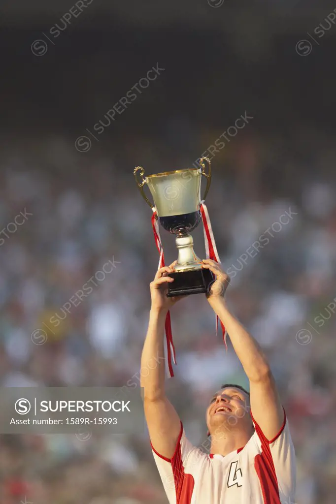 Male soccer player triumphantly holding up trophy