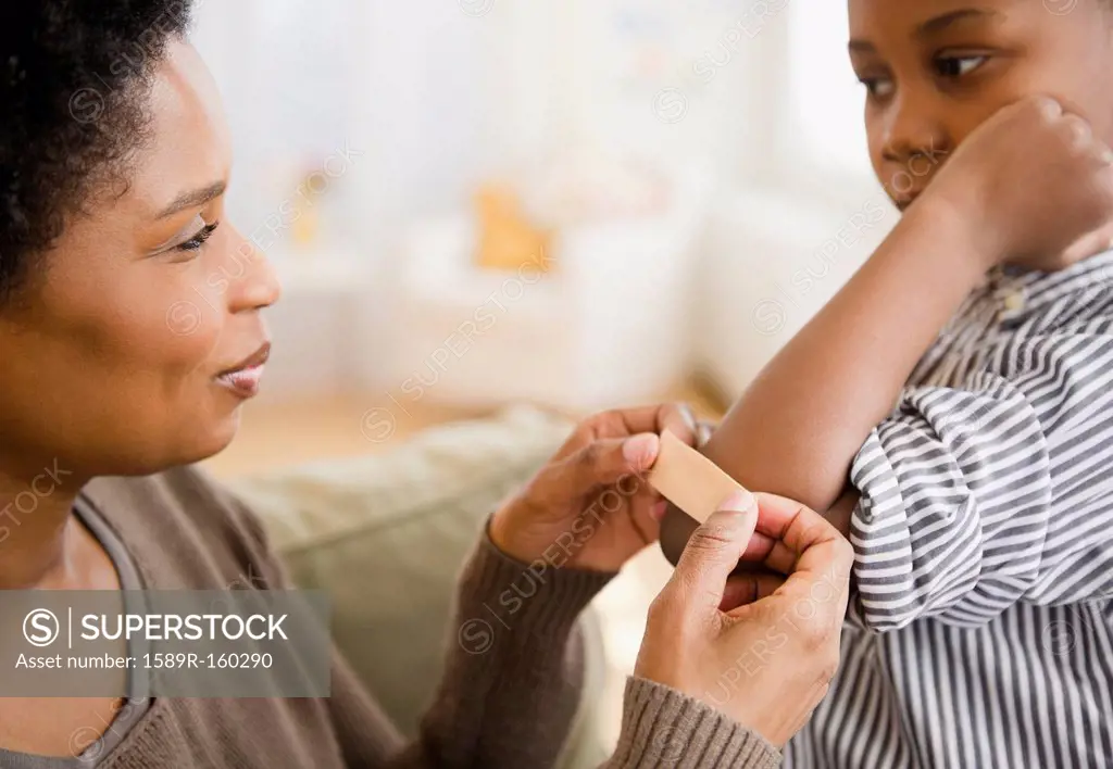 Black mother putting bandage on son´s elbow