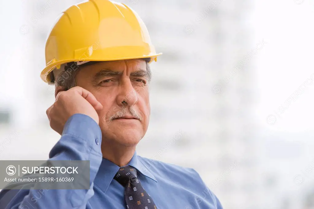 Hispanic businessman wearing hard hat and talking on cell phone
