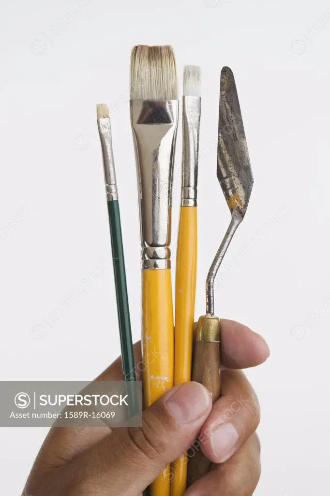 Close up of hands holding paintbrushes and palette knife
